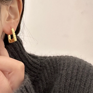 Detailed close-up of a gold-plated square earring with horizontal ribbed texture on a model