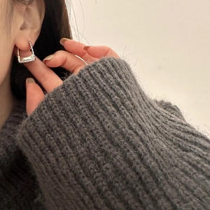 Close-up of silver U-shaped earrings with textured beads on a model in a knit sweater