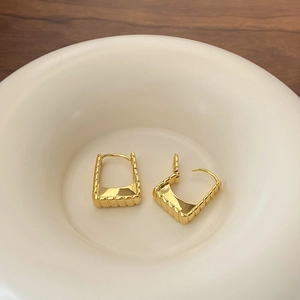 Detail of gold-plated square hoop earrings with ribbed texture on a ceramic tray