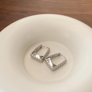 Macro view of silver geometric hoop earrings with textured finish in a ceramic dish