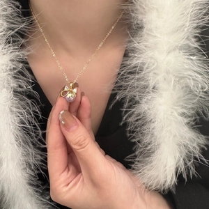 Detail of gold bow necklace with iridescent pearl and zircons on a female model