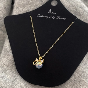 Detail of mermaid pearl pendant with gold bowknot and zircon on a black display card