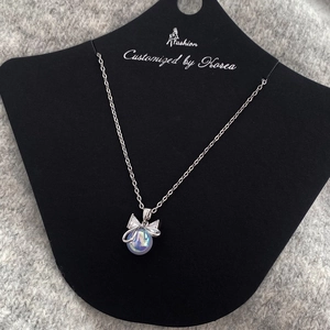 Detail of elegant bow pendant necklace with iridescent pearl on black display card