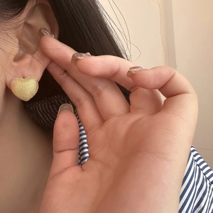Detailed close-up of a textured gold heart hoop earring worn on the earlobe