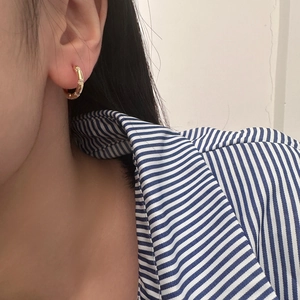 Minimalist geometric gold hoop earrings with small cubic zirconia stones worn by a model