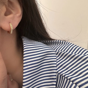 Close-up of geometric gold earrings with micro-inlaid zircons worn by a model
