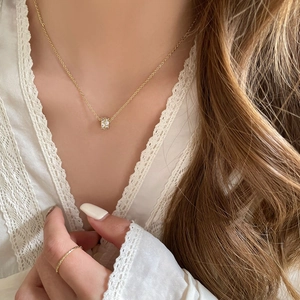 Close-up of sparkling zircon cylinder pendant necklace and thin gold ring on a model