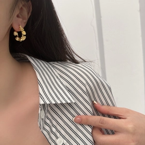 Close-up of gold C-shaped earrings with unique ruffled texture on a female model
