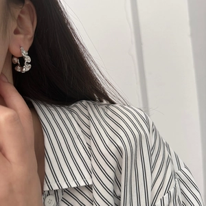 Detail view of silver irregular pleated wave hoop earrings on a model showing modern texture