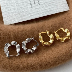 Macro detail of gold and silver plated C-shaped earrings with unique pleated wave texture