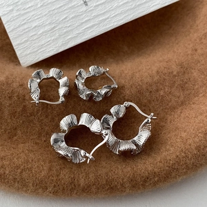 Detailed view of silver C-shaped earrings with ruffled edges on a soft brown background