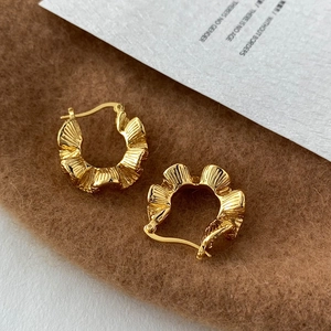 Detailed close-up of C-shaped gold hoop earrings with pleated texture on brown suede