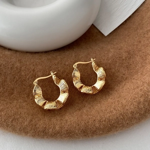 Close-up of C-shaped earrings with 18K gold pleated texture and vintage metal design