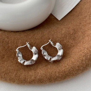 Detailed view of silver C-shaped ruffle texture earrings on a warm brown felt surface