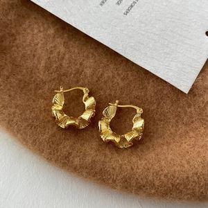 Close-up of gold-plated C-shape hoop earrings with ruffled texture on brown felt fabric
