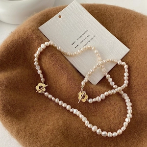 Collana di perle barocche con chiusura a fiore dorato su sfondo di cappello in feltro