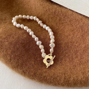 Dettaglio bracciale di perle barocche con chiusura OT a fiore dorato su tessuto