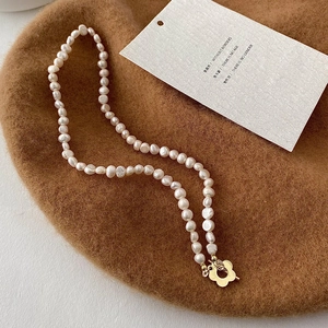 Dettaglio collana di perle barocche con chiusura a fiore dorato su basco in lana
