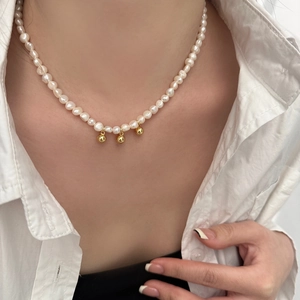 Détail d'un collier de perles d'eau douce avec trois pendentifs boules dorées sur un mannequin