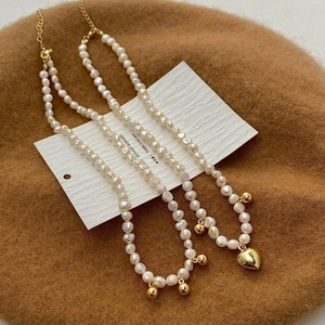 Détail de colliers en perles d'eau douce avec pendentifs cœur et boule d'or sur un chapeau
