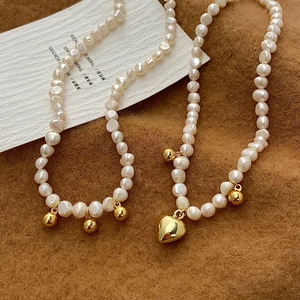 Collier en perles baroques avec pendentif cœur doré sur tissu marron texturé