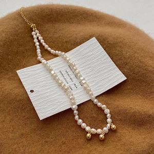 Détail du collier de perles d'eau douce naturelles avec trois perles dorées sur feutre beige