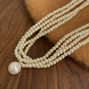 Three-layer rice pearl necklace with a large round pearl pendant on dark textured wood