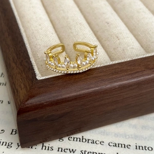 Detail of crown ring with pearls and zircons on a wooden jewelry tray over a book