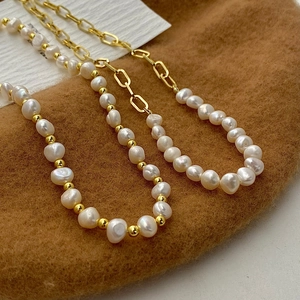 Detail of baroque pearl necklace with golden rectangular links on dark background