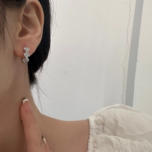 Detail of silver clover earrings with cubic zirconia worn by a model in a side view