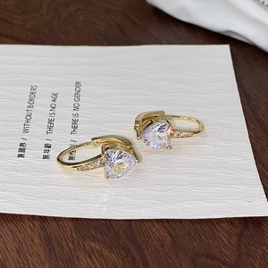 Macro shot of gold-plated heart-shaped zircon earrings on a textured paper background