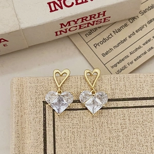 Détails de boucles d'oreilles cœur dorées avec cristaux sur support texturé crème