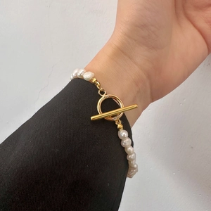 Gros plan d'un bracelet en perles baroques avec fermoir OT doré sur une manche de blazer