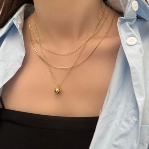 Close-up of triple-layered gold-plated necklace featuring snake chain and gold ball pendant