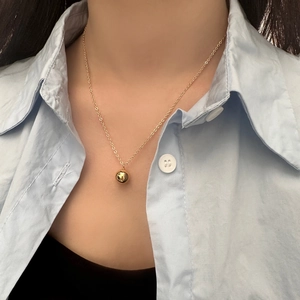 Close-up of minimalist polished gold ball pendant necklace worn with a light blue shirt