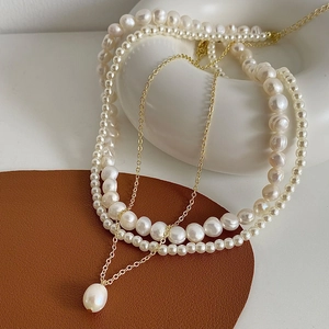 Gros plan d'un collier de perles à trois rangs avec chaîne dorée et perle baroque