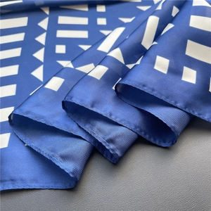 Close-up of silk square scarf featuring royal blue geometric patterns and fine rolled edges