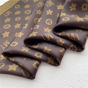 Macro shot of silk satin scarf detail featuring brown floral and letter monogram patterns