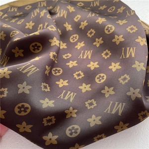 Detail of coffee silk scarf with monogram print and floral patterns on white background