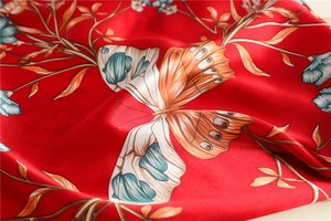 Detailed close-up of red silk scarf showing butterfly and floral patterns with satin sheen