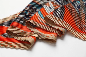 Détail macro du foulard en soie plissé avec motifs colorés et plis accordéon verticaux