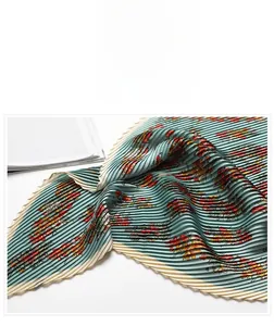 Detail of teal pleated silk scarf showing orange floral patterns and smooth texture