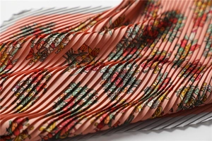 Detailed close-up of fine vertical pleats on a coral silk scarf with floral pattern