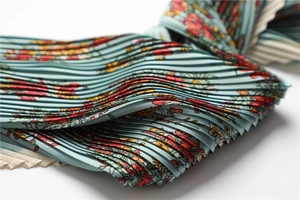 Detailed view of accordion pleated fabric with floral print on elegant teal silk scarf