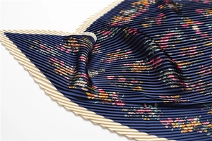 Detailed macro view of navy blue pleated scarf featuring delicate floral patterns and wavy edges