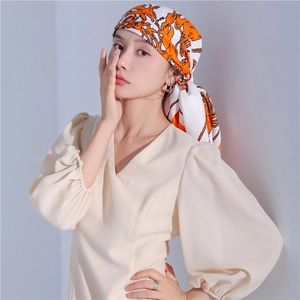 Detail of silk scarf with orange horse pattern styled as an elegant headpiece for women