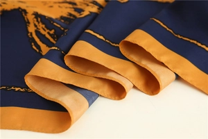 Detailed close-up of navy and yellow silk scarf showing satin texture and rolled edges