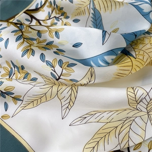 Gros plan détaillé sur la texture soyeuse et les motifs de feuilles jaunes du foulard carré chic