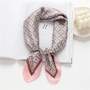 Foulard en soie aux motifs géométriques roses et gris posé sur un magazine de mode