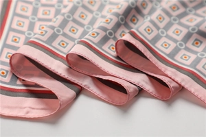 Vue détaillée d'un foulard en soie rose avec motifs géométriques et bordures roulées